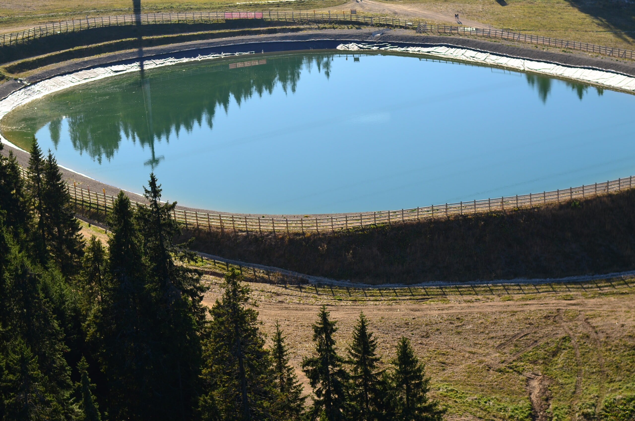 Reservatório artificial de água com revestimento impermeável, cercado por vegetação e estrutura de contenção